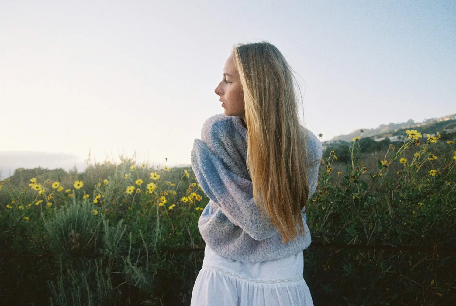 A woman standing in a field of wildflowers, looking into the distance